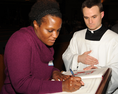 Lilimaria P. Smith, of Prince of Peace Church in Taylors, signs the Book of the Elect during the Rite of Election. At right is Father Bryan Babick, diocesan master of ceremonies. The Piedmont deanery rite was held at St. Mary Magdalene Church in Simpsonville on Feb. 19.