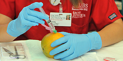 Sophomore Emily Corbett practices giving shots by injecting a saline solution into an orange. (Roper St. Francis Healthcare/Joan Perry)