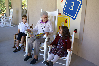 (Photo provided) Parish volunteer Stella Heuer reads to pre-K students on the front porch of St. Gregory the Great School’s new Cottage in the Woods Early Childhood Center.
